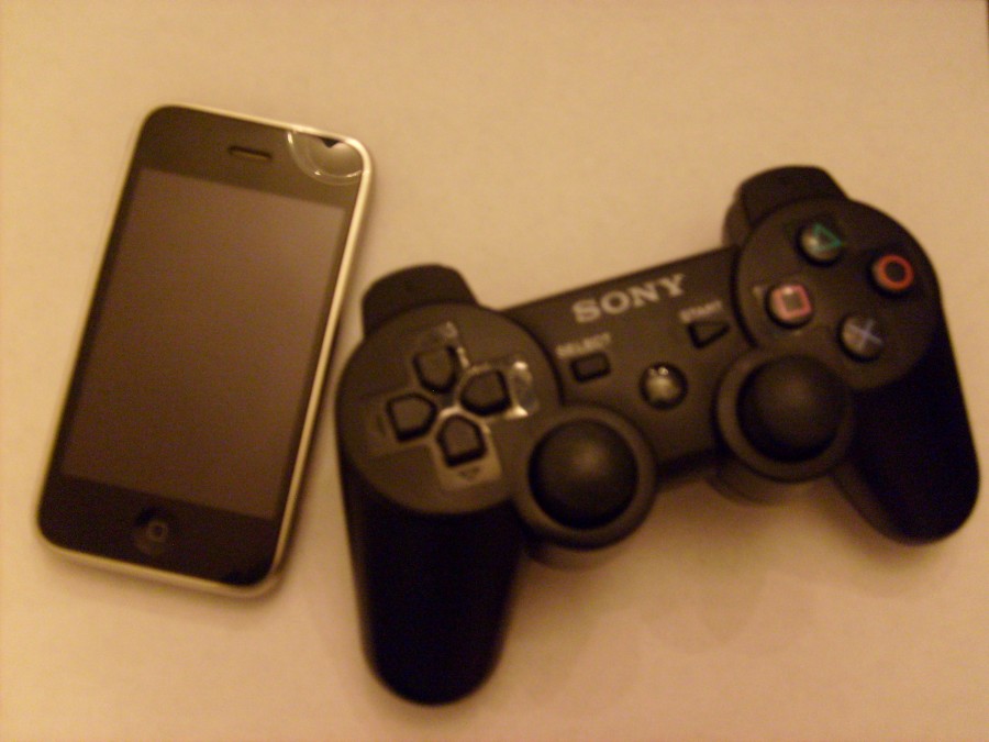 The+comparison+of+simple+and+complex%3A+an+iPhone+sits+next+to+a+Sony+Play+Station+controller.
