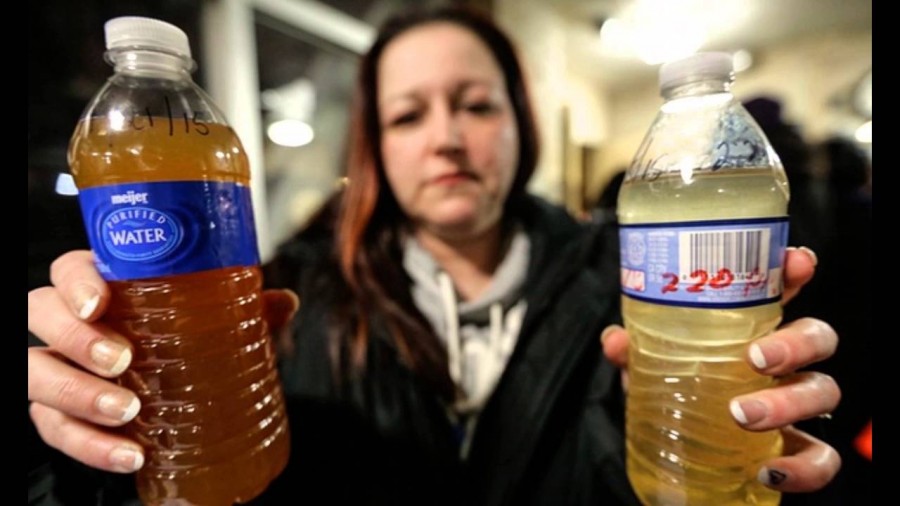 A woman holds up bottles filled with the poisoned water that has been circulating through Flint, Michigans water pipes.