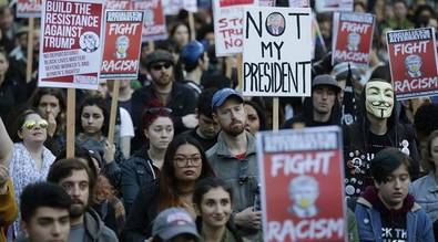 People hold signs as they listen to speakers at a protest agai