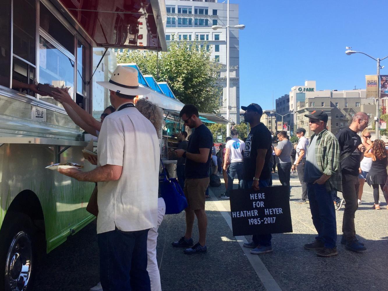 Peaceful protesters stand in line to buy food from a food truck at the rally. One man holds a Here For Heather Heyer sign.