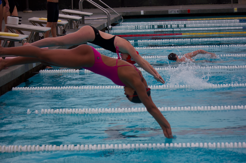 Two girls trying out for varsity dive into the pool to start their warm-up laps.