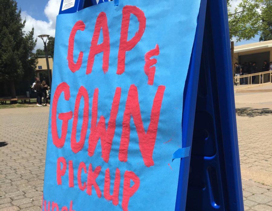 A sign displayed in the quad shows seniors where to go to pick up their caps and gowns.