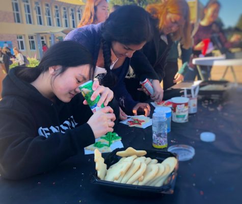 Soni Kanaya and Chloe Palarca-Wong, both juniors, participate in one of the Holiday Village activities by decorating cookies in the quad.
