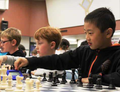 A boy reaches to hit the timer, signaling the end of his move against his opponent. 