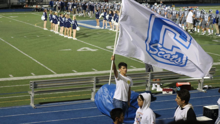 ASB member Nate Rutter waves the Carlmont flag for the crowd as the cheer and football teams meet on the field.