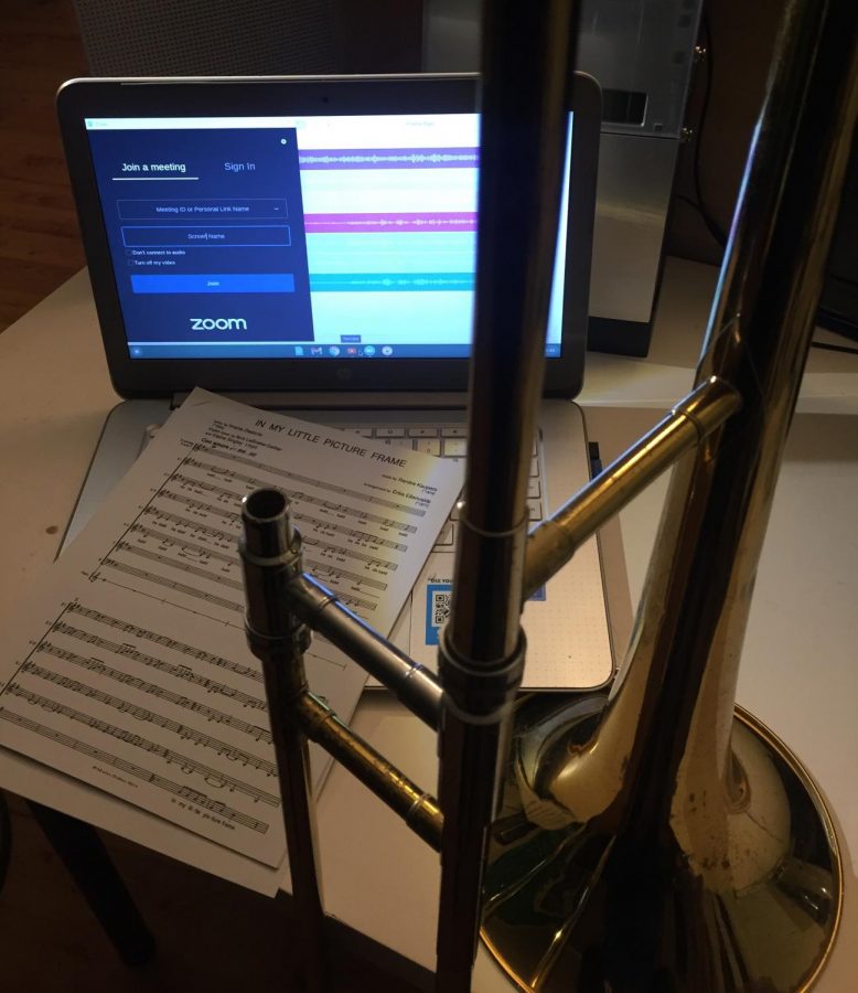 A computer open to Zoom and Soundtrap with sheet music and a trombone next to it.