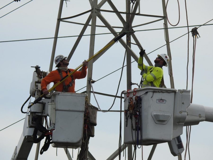 Two Pacific Gas and Electric (PG&E) workers hook a wire to an electrical tower near the Redwood Shores Levee.
