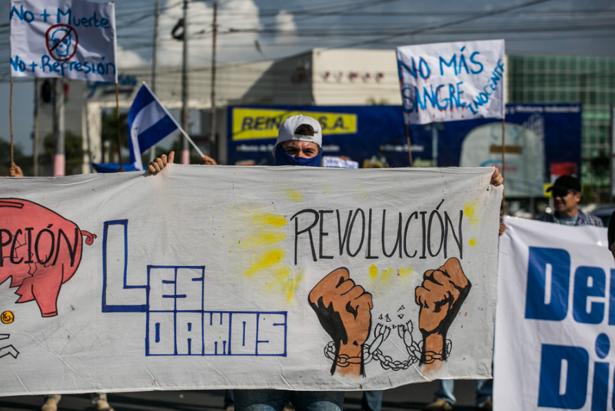 At a student protest in Managua, a masked protester holds a banner calling for a revolution.