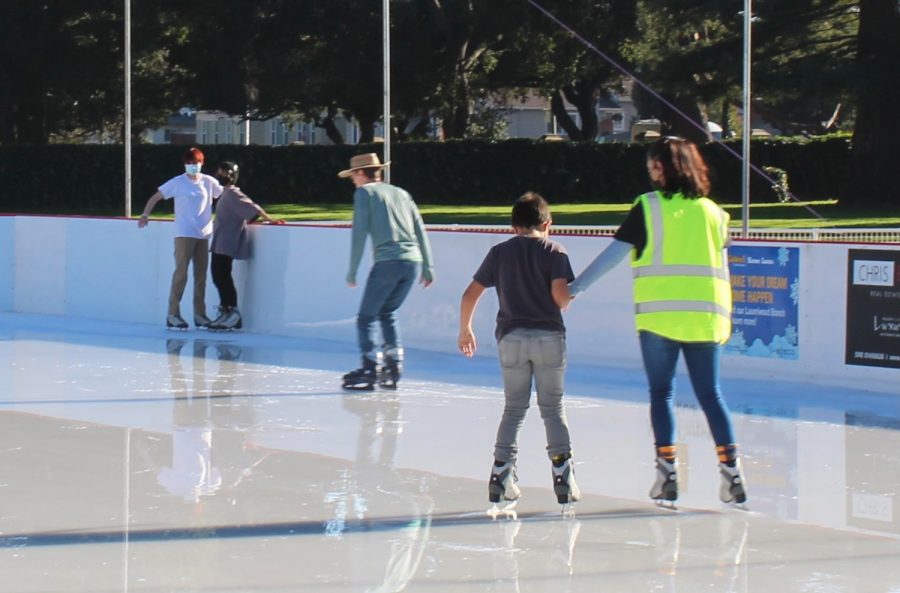 A worker at San Mateos Central Park ice rink helps a kid skate around the rink. 