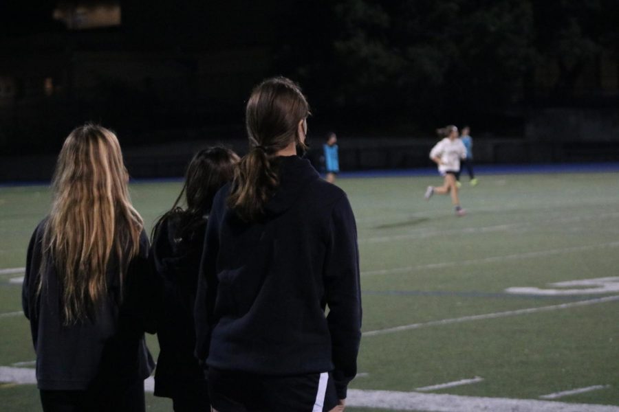 Injured players on the Carlmont JV girls soccer team watch their teammates practice from the sidelines.