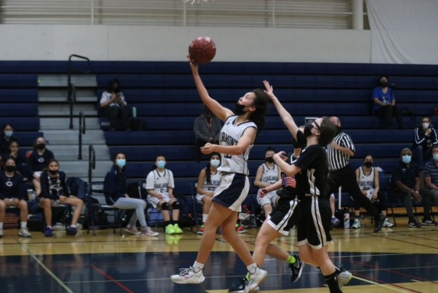 Sophomore Charlotte Lin hurls the ball towards the basket during a layup as two Ravens anticipate a rebound.