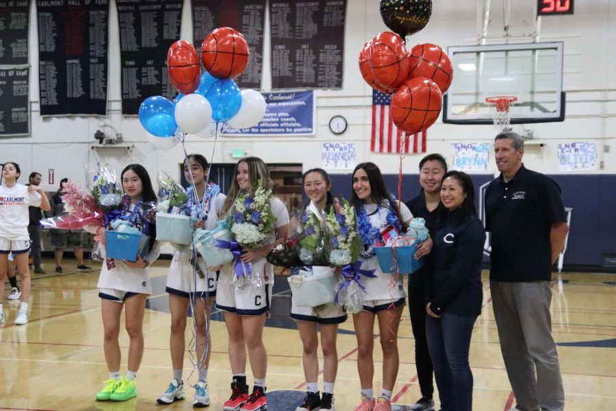Varsity girls basketball seniors gather with their coaches for a photo.