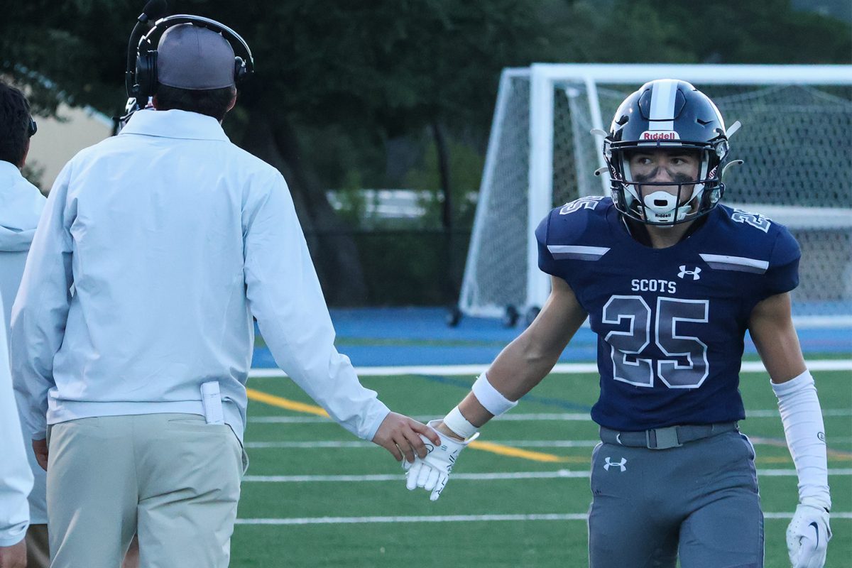 During the first quarter, junior defensive back Keoki Firenze intercepted the ball. He celebrated with his team on the field after making the play. His coach high-fives him as he walks to the bench.