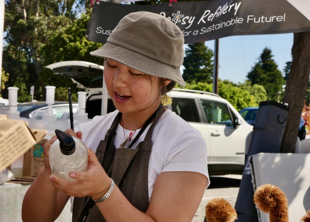 Karen Chaw, the owner of The Daisy Refillery, labels a jar filled with lavender body wash for a customer at her South San Francisco Farmers Market booth.
