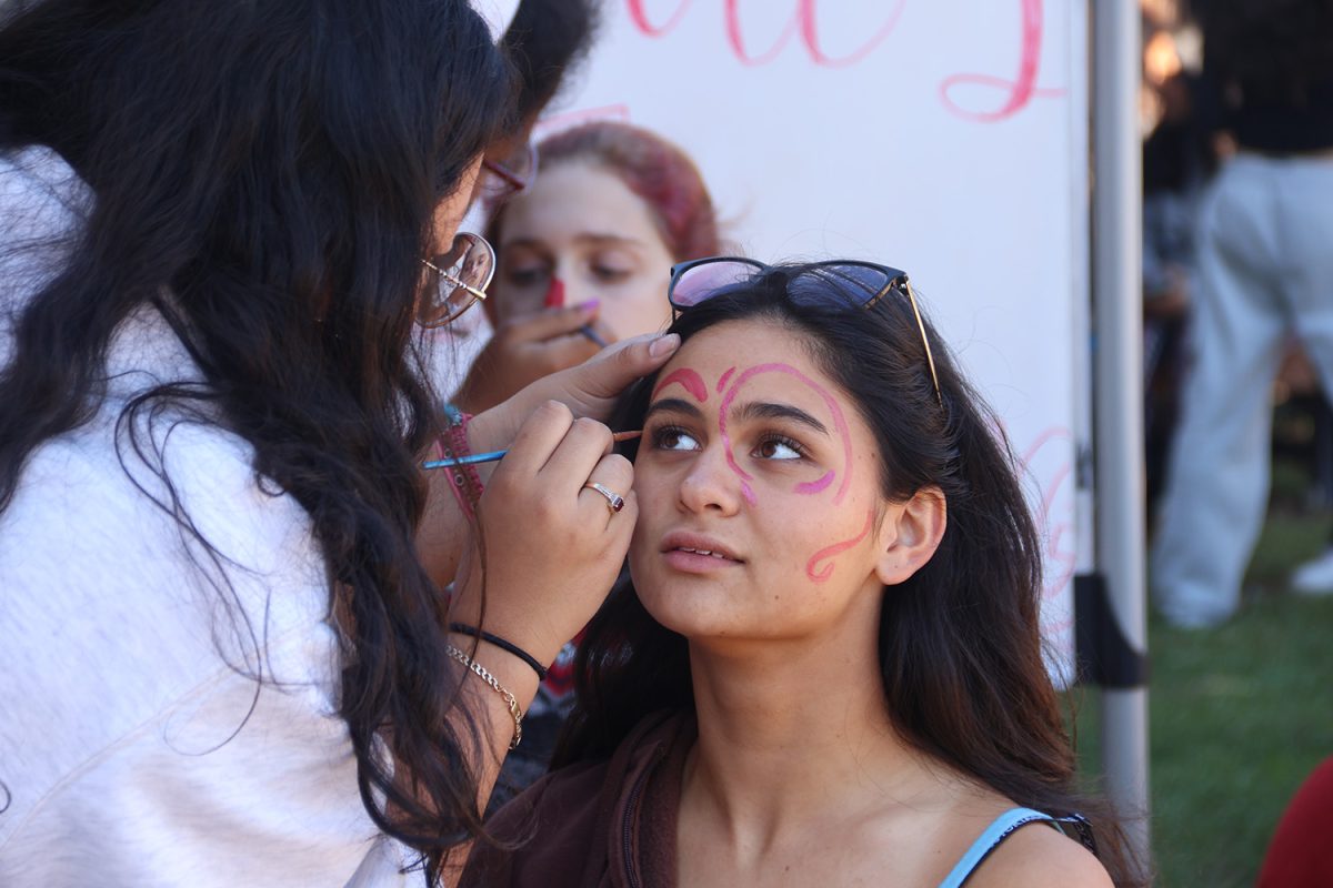 Junior Mattie Llido gets her face painted by junior Kimberly Garcia during lunch on Friday. Garcia is a member of the Latinos Unidos Club, which hosted a face-painting activity for Dia de los Muertos. Many students gathered around for the free candy and face paint that the club offered.