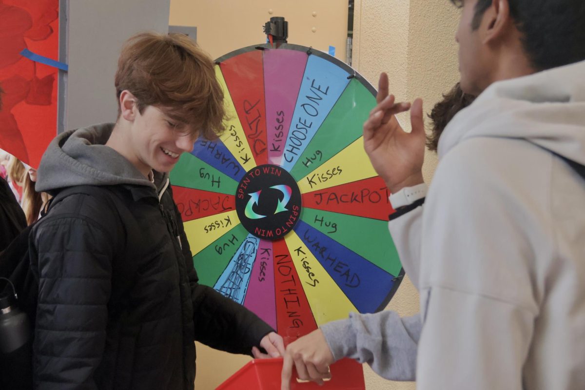 Senior Aaron Jedrzejek participates in the spin-to-win-wheel at the hugs and kisses booth. Winning a chocolate kiss, Jedrzejek happily claimed his prize from the bin. Located in the quad, many Scots took turns spinning the wheel, hoping for the best prize. 