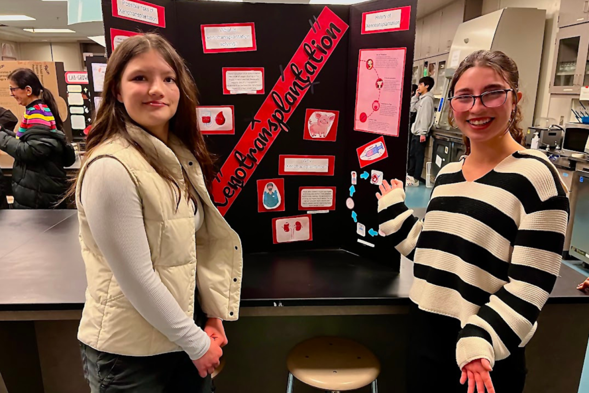 Sophomores Lily Hinde and Isa Haggarty pose beside the xenotransplantation presentation they created for BTI. Students got to choose a topic that demonstrated biotechnology in the real world and present their discoveries during open house.