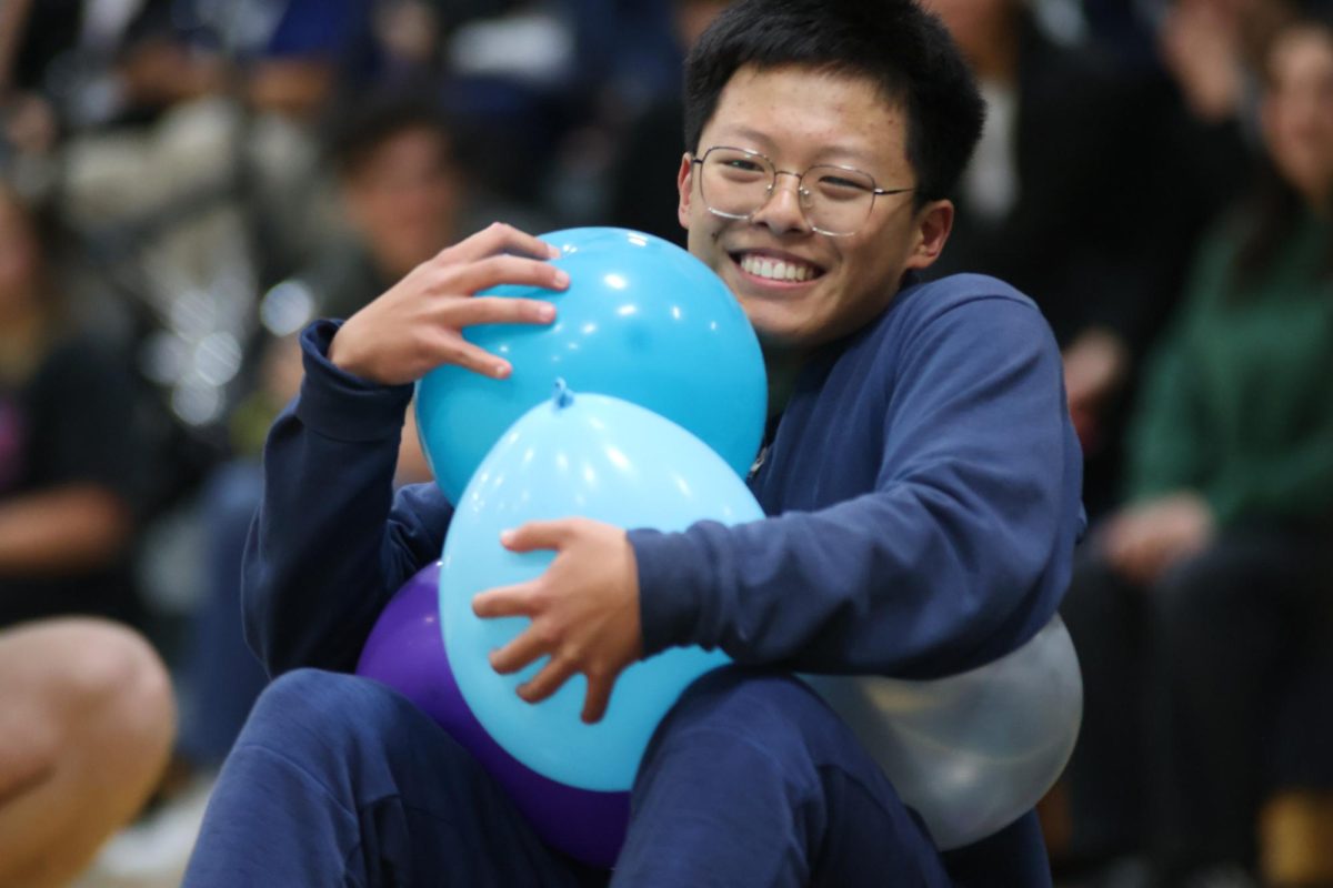 Sophomore Kevin Li grins as he scoots towards more balloons to grab. Several players had difficulty grasping multiple balloons in the competition and often lost control of them. 
