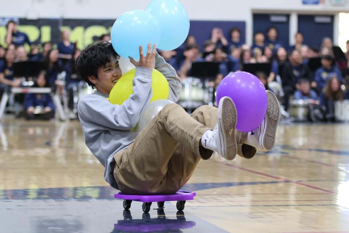 Senior Max Weitzman balances on a floor scooter, anxiously maintaining a grip on all the balloons he gathered. During the Heritage Fair, one student from each grade got the opportunity to participate in a balloon battle. Moving around using the floor scooters, players had to compete against one another to see how many balloons they could hold onto. The winners received a box of Lucky Charms cereal. 