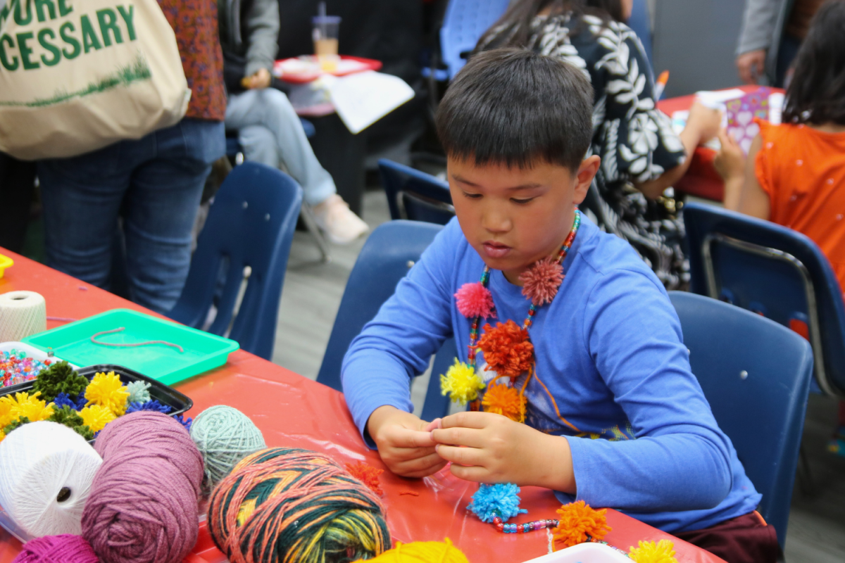 A boy makes a beaded pompom necklace in the craft room. He used the array of provided materials for his creations. There was also a station to make personalized Mothers Day cards.