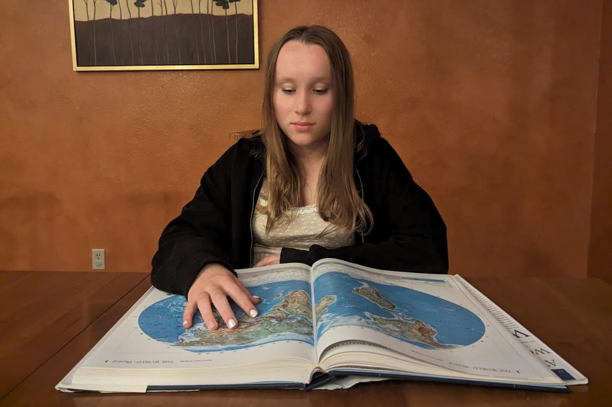A student sits at a table, examining a map of the world. Geography classes are not required in many American schools, resulting in a concerning lack of geographic knowledge in students.