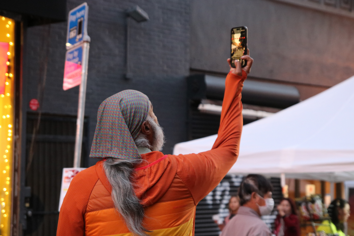 A man takes a photo of the sunset. He stood at the first block of the night market, capturing the aesthetic view of the red-lit lanterns against the orange tinted sky. The sun set at around 8 p.m., which was an hour before the market closed.
