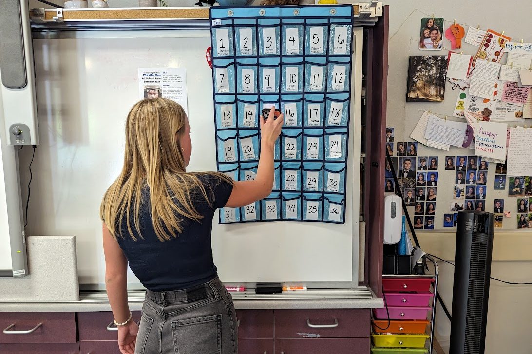 A student places her phone in the phone pocket in her classroom. Each pocket is labeled with numbers and students names in each period, so the teacher can ensure all students phones are accounted for and simultaneously take attendance.