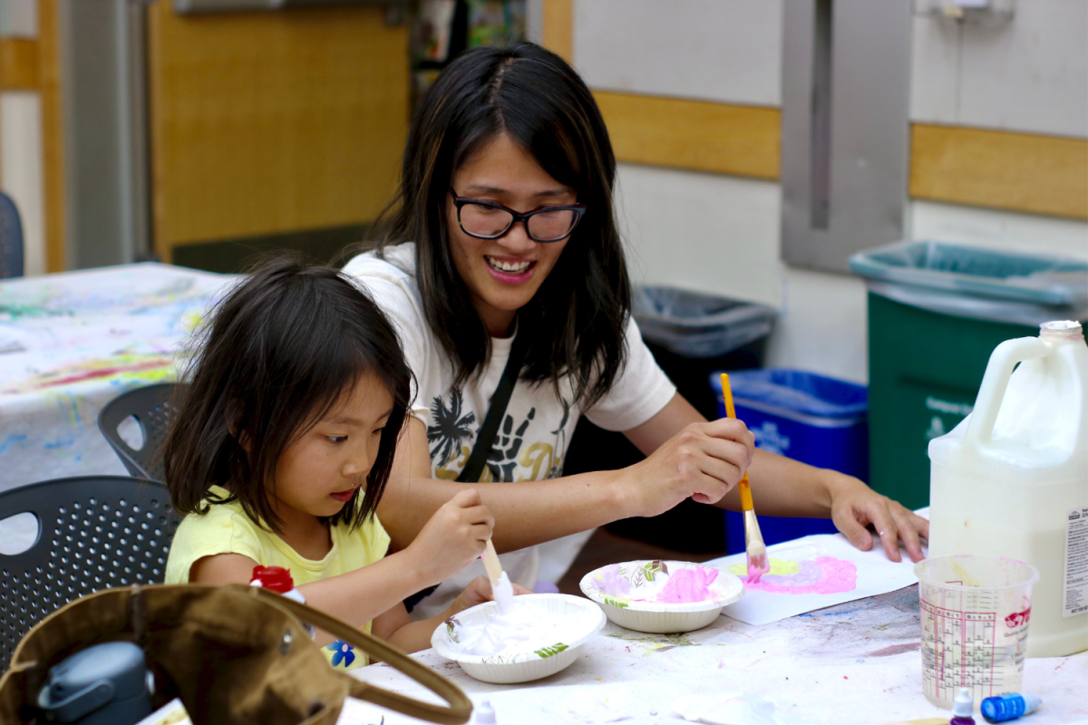 Lan He watches her daughter mix shaving cream into her bowl of paint. To create different colors, they added food coloring to their mixtures. During the Crafternoon, they painted rainbows together. 