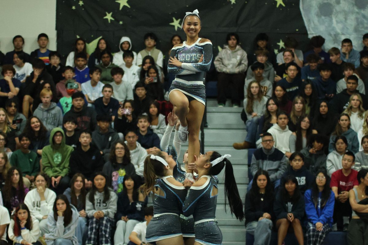 Junior Quincy Leong hits her position midair during the varsity cheer team's performance.