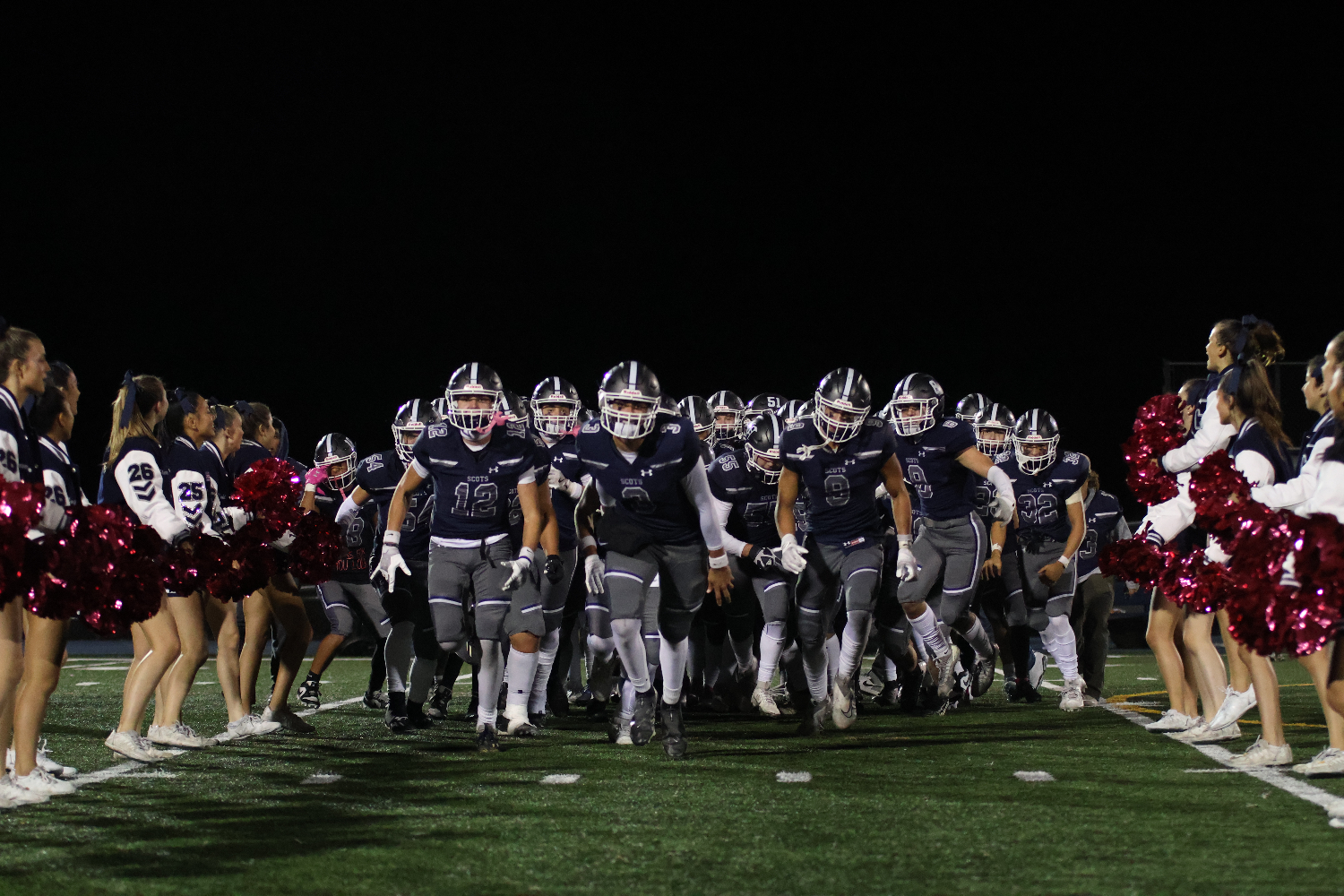 The varsity football team runs down a row of enthusiastic cheerleaders, celebrating their 42-38 win. 