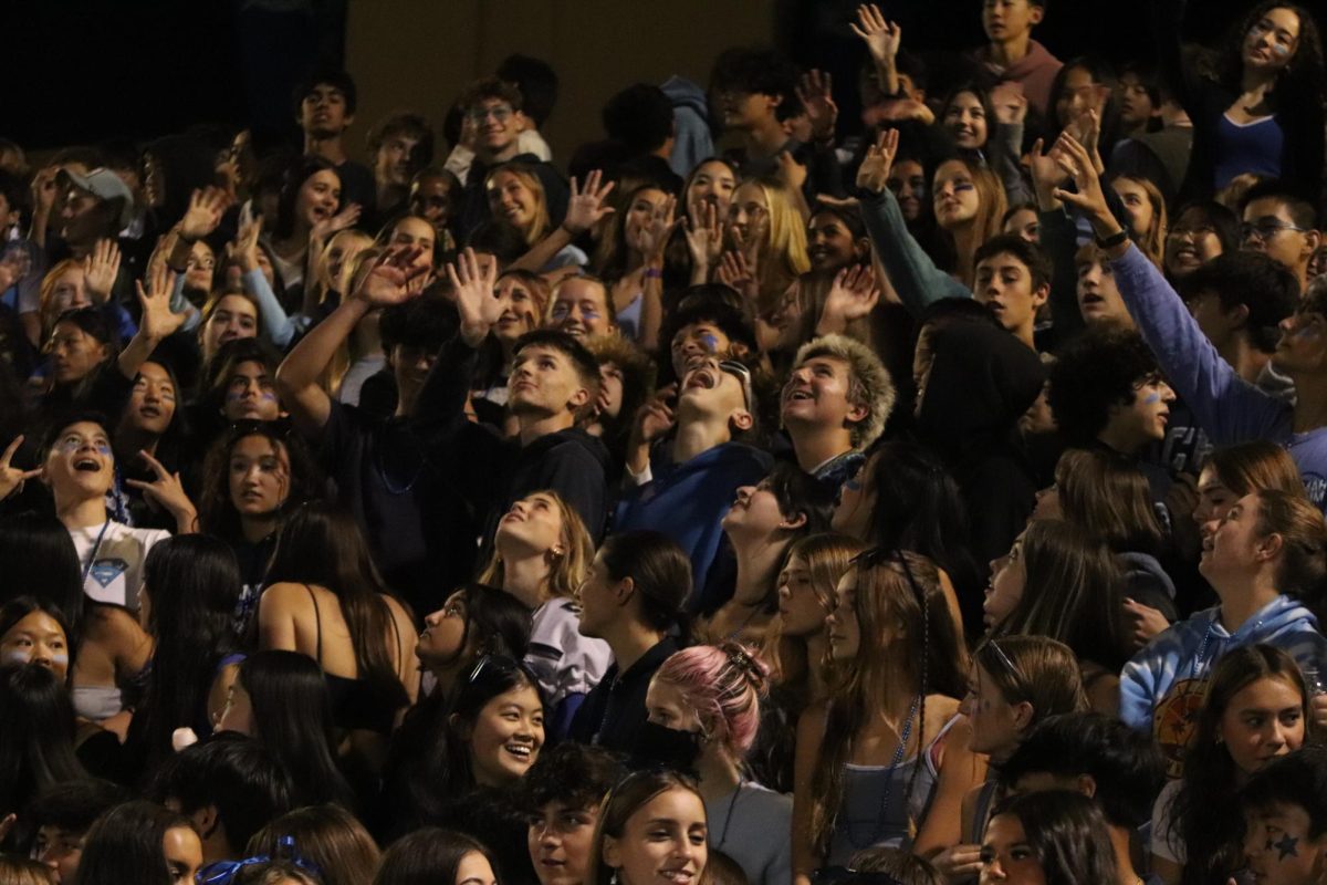 The student section look towards the sky as they wave to the drone above. 