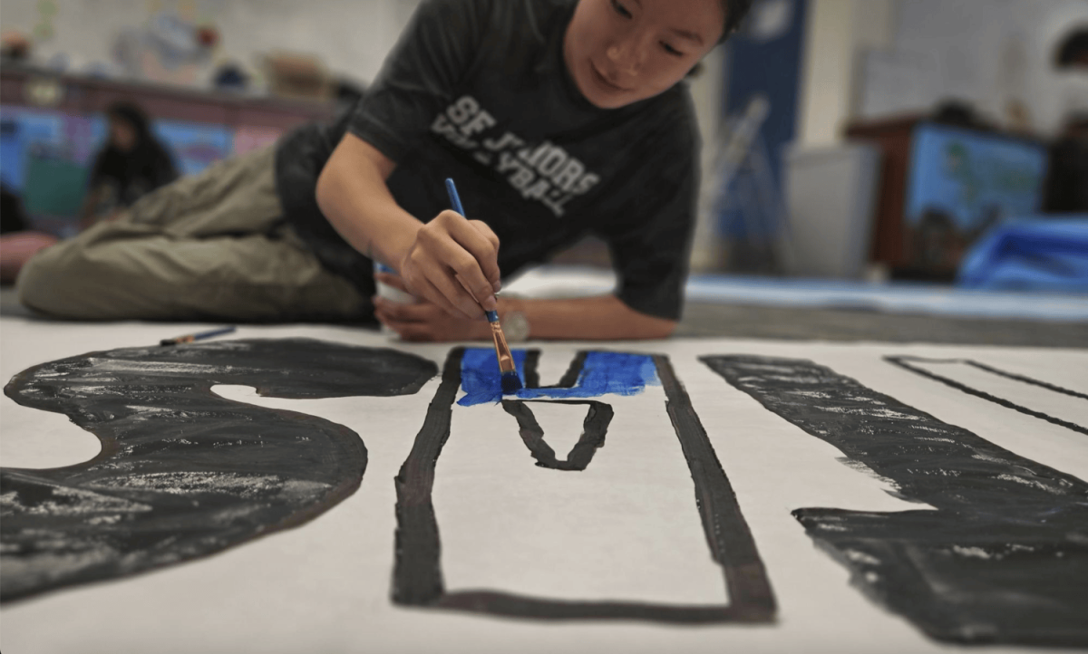 Positivity Commissioner Jaysie Ho paints a banner for Milpitas High School, welcoming them to Carlmont for the homecoming game. 