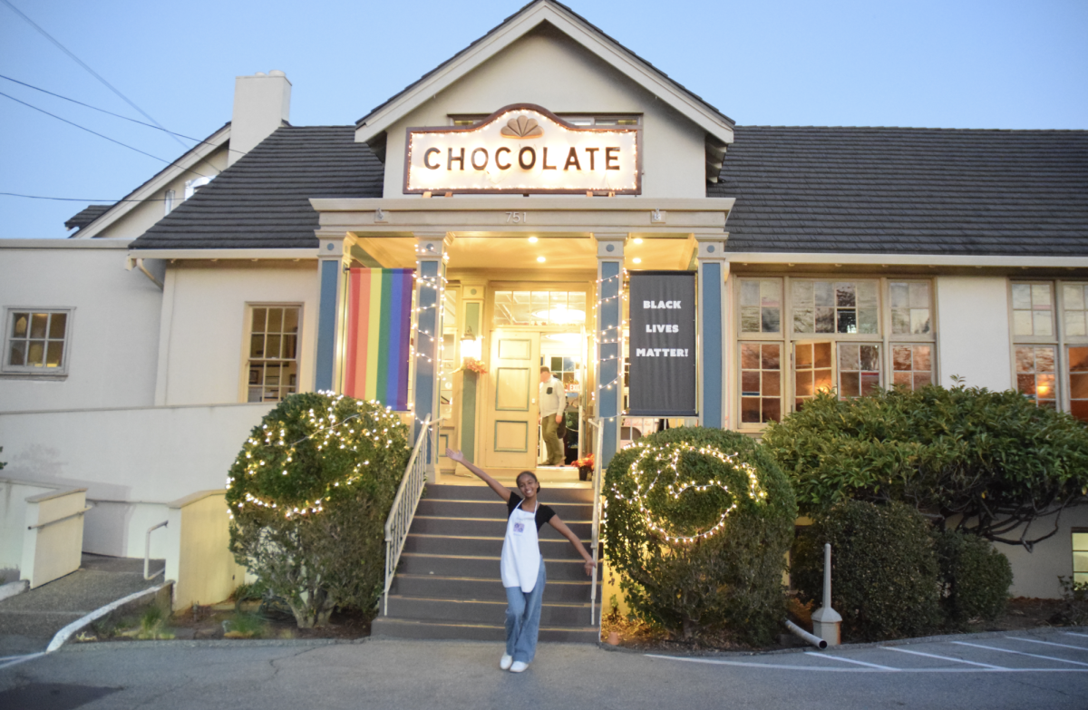 A photo of the Chocolate sign outside of the church with community volunteer Naomi Dulac. The sign was originally built by Bob Donavan, who is now 103 years old and has been a member of the church for 64 years. He built the sign for the second-ever Chocolate Fest and it has been happily displayed above the church for the past 40 Chocolate Fests. “Nobody asked him to do it, he just said, well we need something that can be seen from the street,” said Michelle Carter, the first organizer of Chocolate Fest.