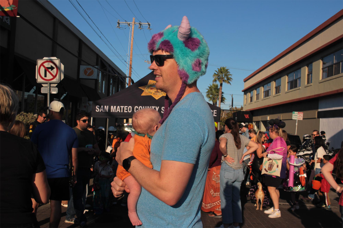 A dad dressed as Sully from Monsters Inc. holds his baby dressed as a pumpkin.