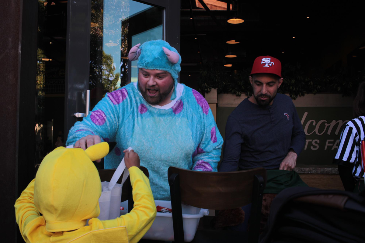 A man dressed as Sully from Monsters Inc. hands out candy to a little boy dressed as Pikachu from Pokemon.