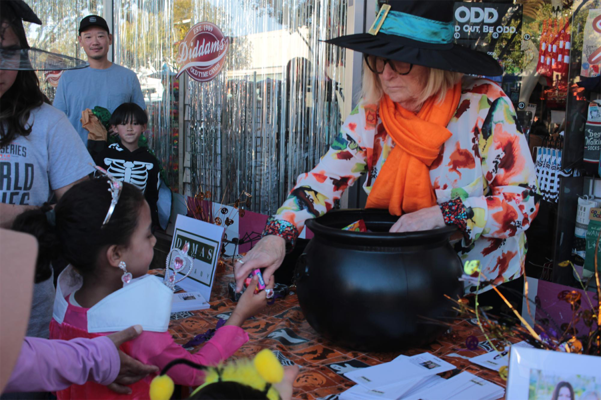 A woman dressed as a witch hands out candy in front of Diddams Party & Toy Store.