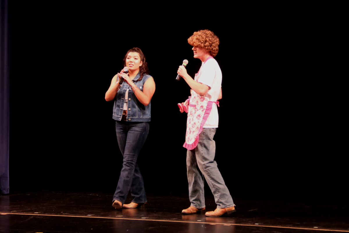 Rhaya Szego dresses in a jean vest and pants and August Steunenberg wears an apron, carrying a doll in his right arm as they sing "Mr. Mom" by Lonestar. The song is about a man's new life taking care of his children while his wife works.