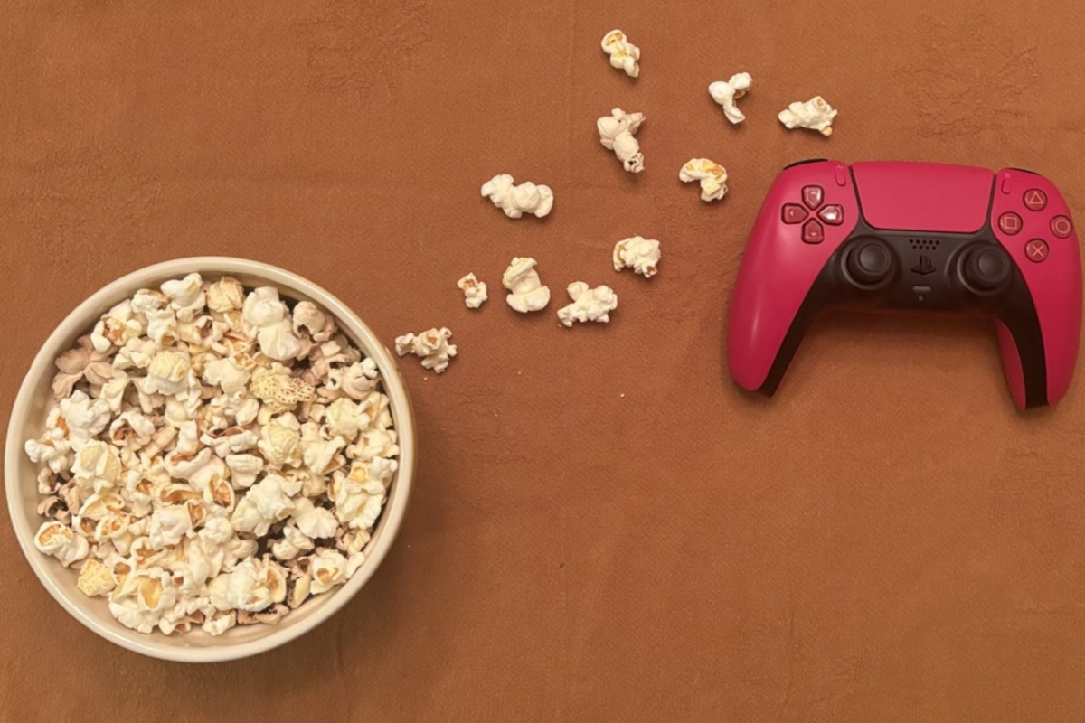 A bowl of popcorn and a video game controller lay beside each other. Crossovers between video games and film are becoming increasingly prominent within the film industry.