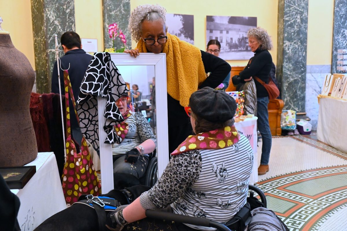 Jerri Scaife helps a customer try on one of her scarves. Scaife is the owner of JerrisCreations and has been designing since the age of 12, creating textiles from scarves to wraps to dresses. 