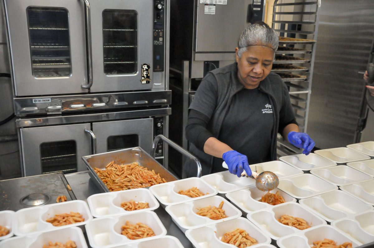 Food services worker two, Mariana Pavon, scoops pasta into individual containers. Pavon cooked the pasta in a large pot and then poured a large can of tomato sauce on top before mixing it. Workers must ensure that the food is ready to eat and healthy, which the team ensures by taking the temperature of the food and using low-sodium pasta sauce.  