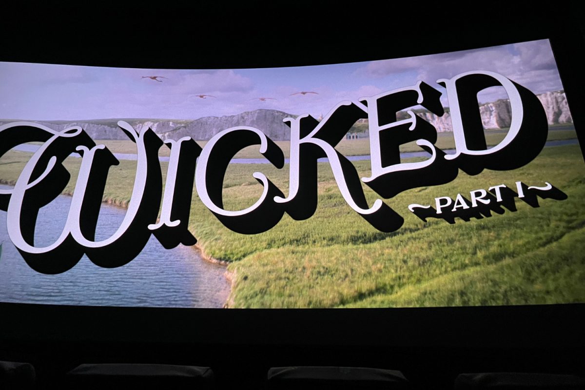 The "Wicked" movie logo is displayed on a movie theater screen.