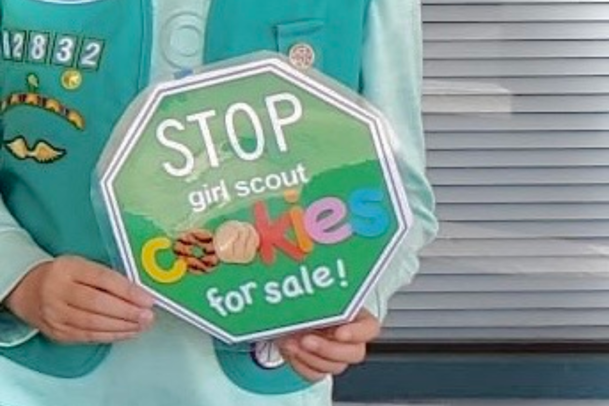 A Girl Scout is holding a sign encouraging customers to buy Girl Scout Cookies. "I've seen some Girl Scout cookie booths have fun marketing techniques, like doing dances and singing songs," Shah said.