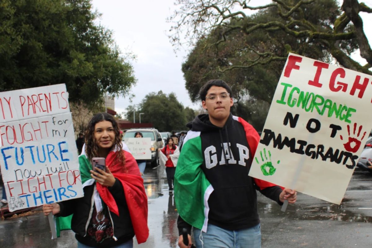 Latino students exiting Menlo Atherton's campous and entering the streets to stand up for justice. Two students are seen carrying posters in the rain while wearing Mexican flags over their bodies
