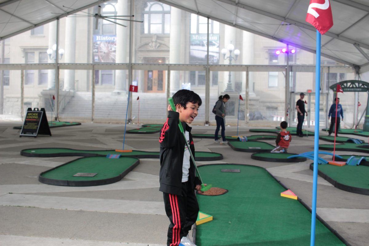 A young boy sports a bright smile as he celebrates his great shot at Redwood City's temporary mini golf course. 