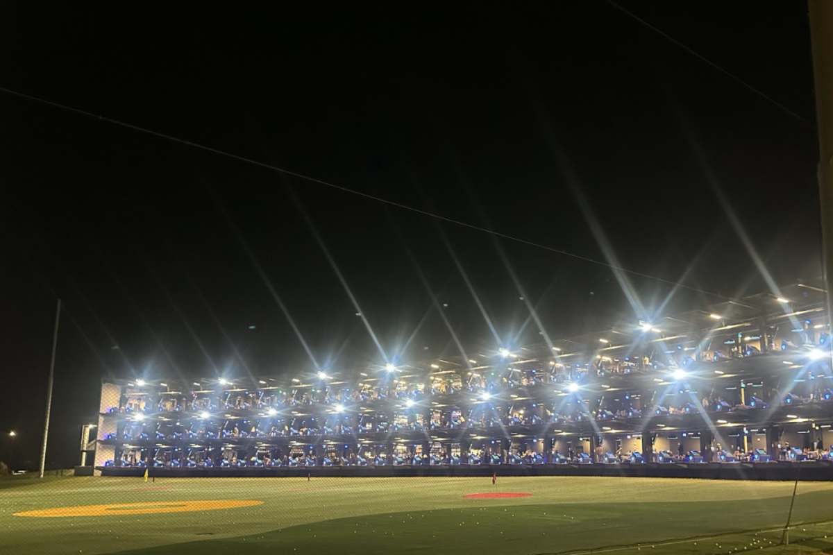 The Topgolf facility brightens the sky on a Friday night. Three stories of occupied golfing bays are visible. Topgolf uses microchipped golf balls to track accuracy and distance, adding a high-tech twist to the game.