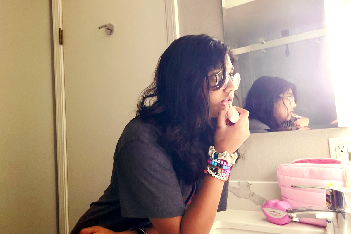 A girl stands in front of a mirror, doing her makeup and trying to perfect her lipstick by leaning into the mirror. Many girls follow tutorials promising they will teach them how to glow up. However, such promises tend to decrease girls' self-esteem as they become used to thinking that they are ugly.