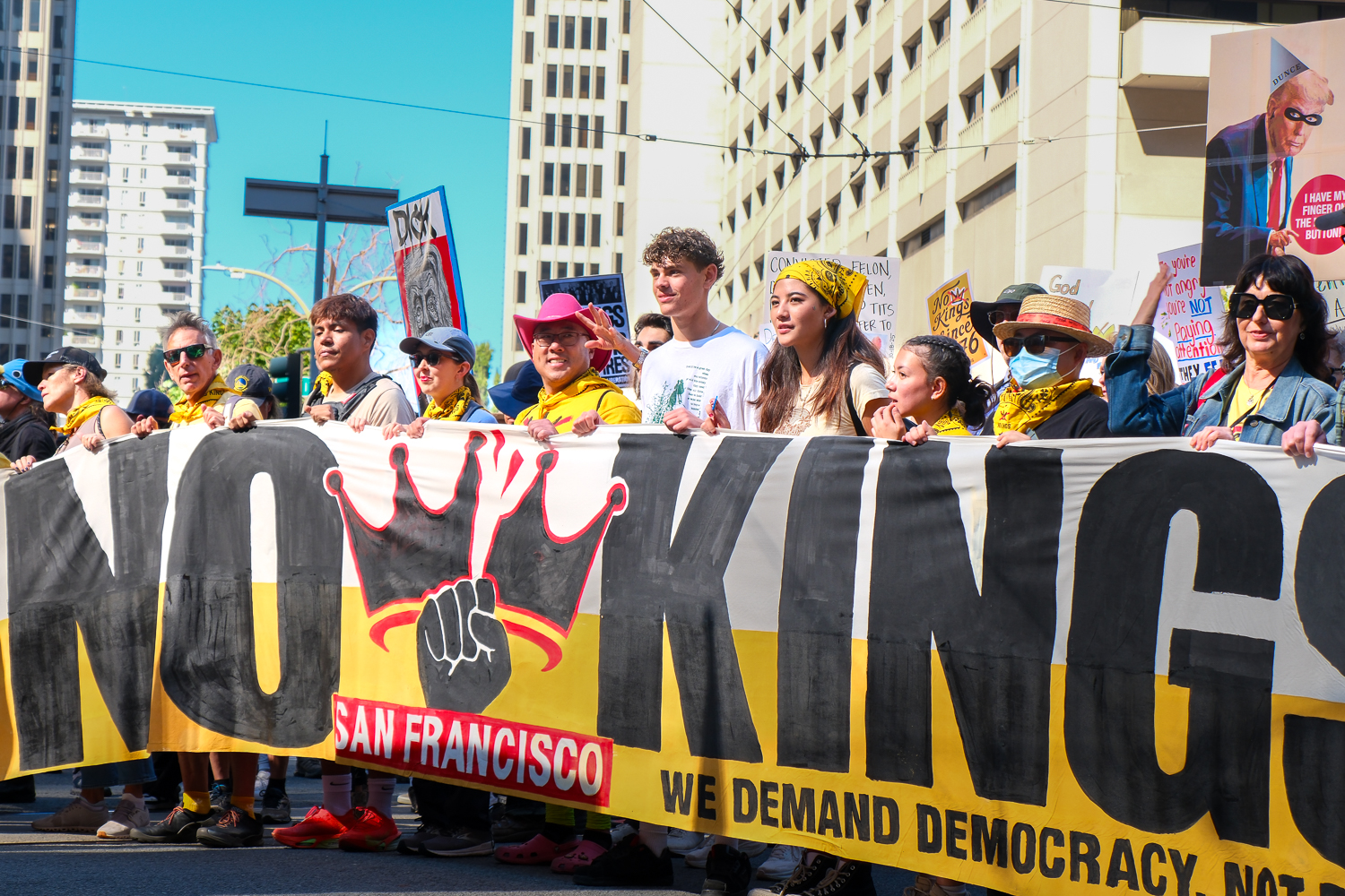 A row of protesters proudly hold a bold "No Kings" banner, ready to lead the many thousands of marchers gathering on Market Street. It was the first of many thousands of signs raised as the crowd moved toward the Civic Center. "No Kings being my first protest feels like coming full circle because it connects to so many things I care about," said San Francisco State University freshman Biel Cardona.