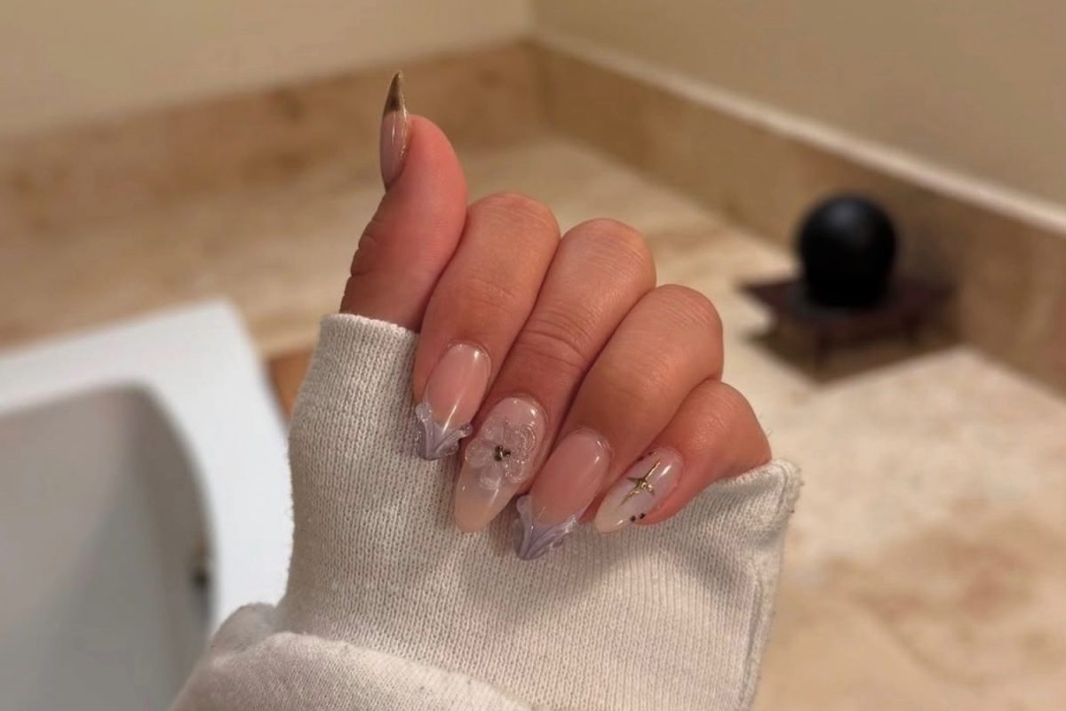 Purple themed nails painted by Kara Lee. There are purple French tip designs and sculpted flowers on the nails. 