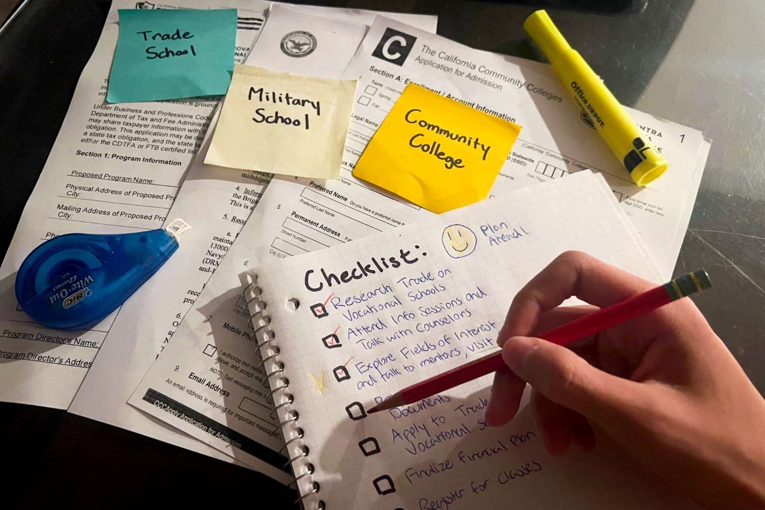 A student checks off another item on their post-graduation planning checklist, weighing down a growing stack of applications. The pile highlights the range of options available to high school students beyond the traditional four-year college route, as well as the increasing number of students considering alternative paths. 