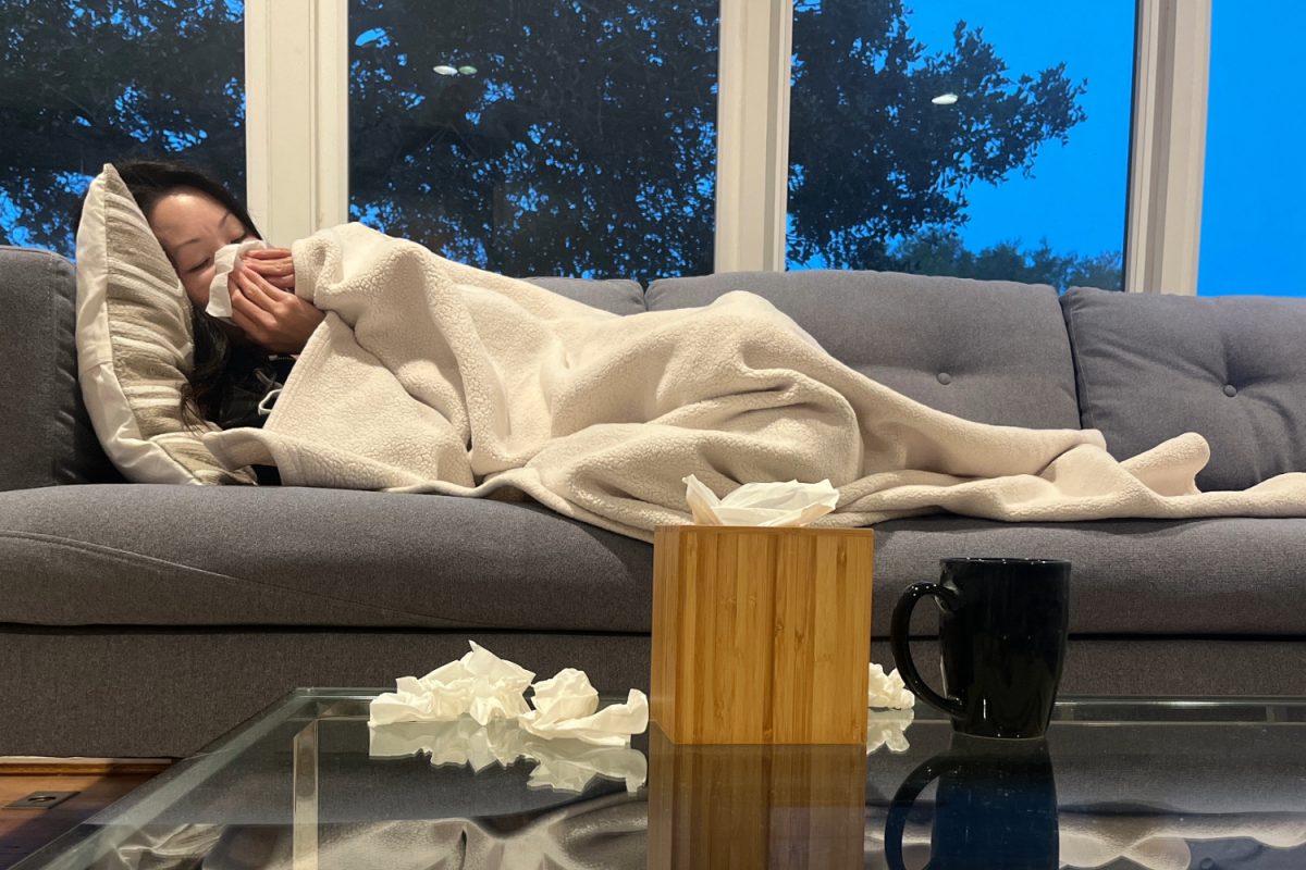 A woman rests on a couch at home while experiencing flu symptoms, using a tissue as she recovers from illness. Health officials recommend staying home when sick to reduce the spread of viruses. "Stay home when you're sick," said San Mateo County (SMC) Health educator Tamta Mchedlishvili.